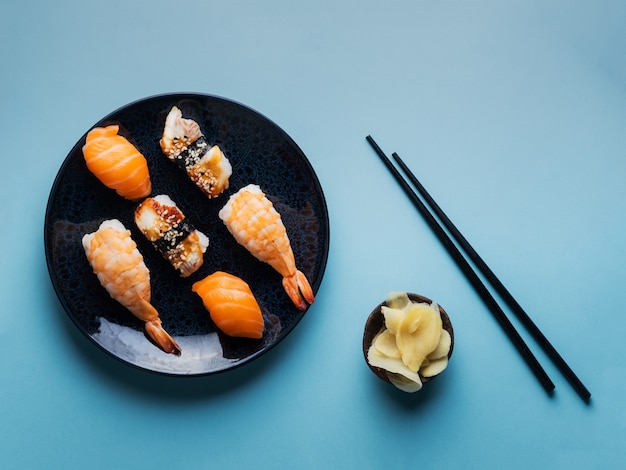 Delicioso y apetitoso juego de sushi servido en un plato de arcilla con salsa de soja y palillos planos en azul