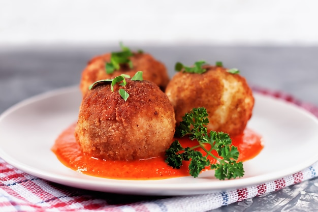 Delicioso arancini italiano quente - bolinhos de arroz recheados com queijo em molho de tomate, em um prato sobre uma velha mesa de madeira