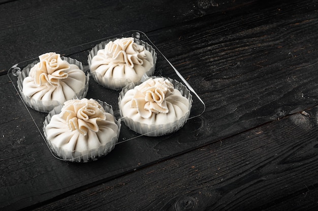 Delicioso baozi, conjunto de pão chinês de carne cozida no vapor, em bandeja de plástico, no fundo preto da mesa de madeira, com espaço de cópia para o texto