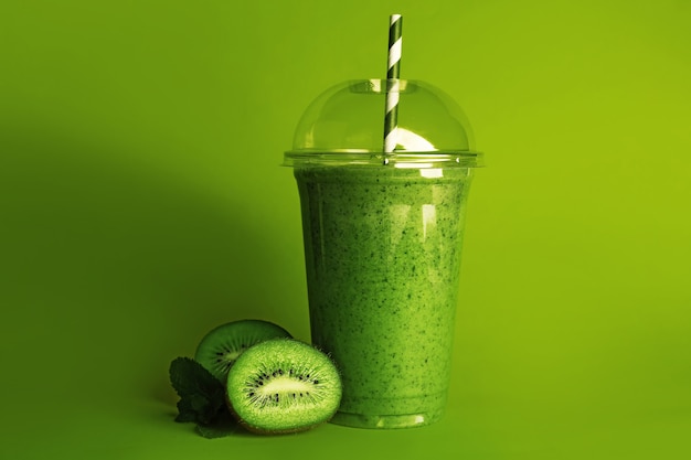 Delicioso batido de kiwi en vaso de plástico sobre superficie verde