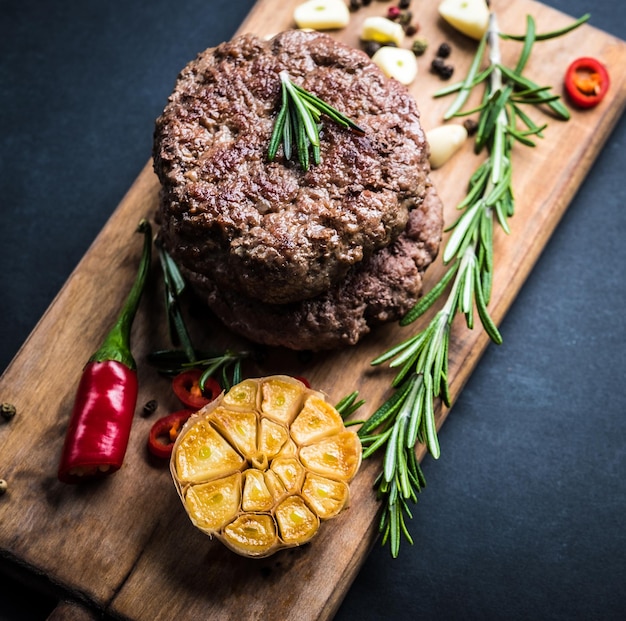 Delicioso bife de hambúrguer de carne com especiarias e ervas na placa de corte e vista superior de fundo de ardósia