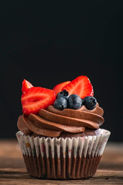 Delicioso bizcocho de chocolate con crema decorado con fresas y arándanos Muffin sobre fondo negro marco vertical Copiar espacio
