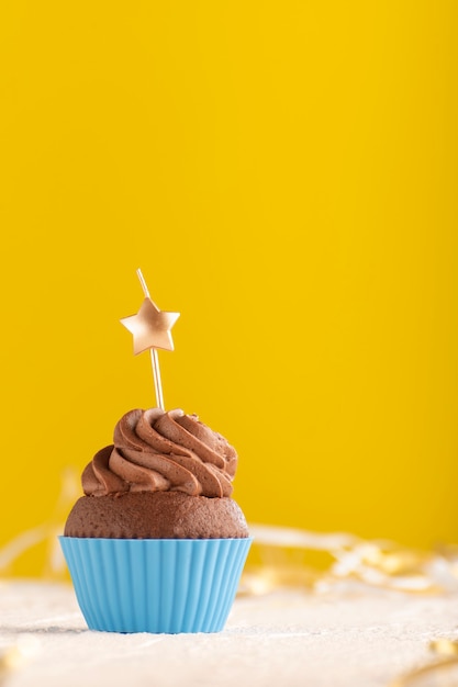 Delicioso bolinho de chocolate com cobertura de creme de manteiga com velas em forma de estrela sobre fundo amarelo. Moldura vertical