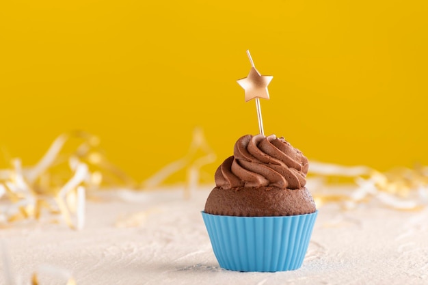 Delicioso bolinho de chocolate com cobertura de creme de manteiga com velas em forma de estrela sobre fundo amarelo.