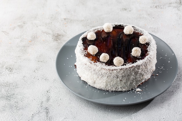 Delicioso bolo de chocolate inteiro no prato com doces de coco em cima na mesa no fundo de mármore. Papel de parede para café de pastelaria ou menu de café. horizontal.