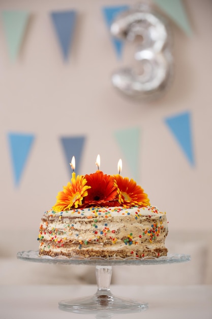 Foto delicioso bolo de creme branco no estande decorado com flores frescas e velas no aniversário