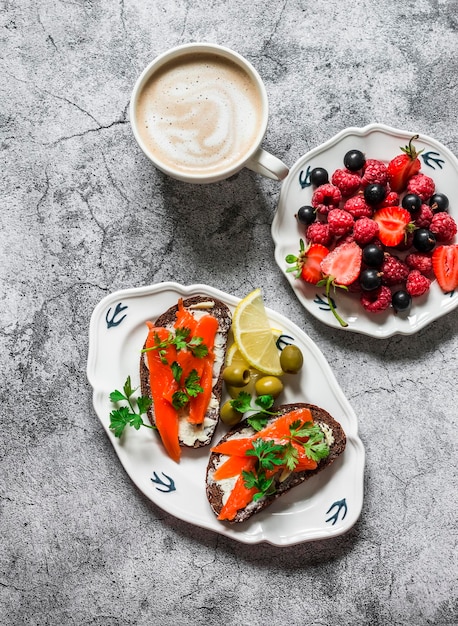 Delicioso brunch de desayuno o bocadillos de capuchino con bayas de salmón en una vista superior de fondo gris