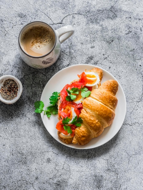 Delicioso café brunch con sándwich de crema y croissant con salmón con queso crema y huevo hervido en una vista superior de fondo gris