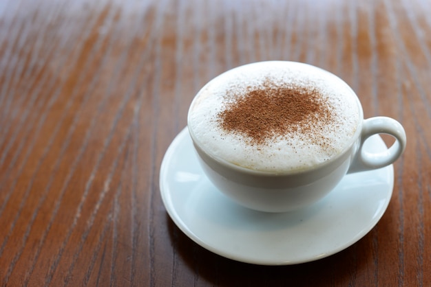 Delicioso café caliente con capuchino caliente en una taza blanca en un restaurante en una mesa de madera con canela