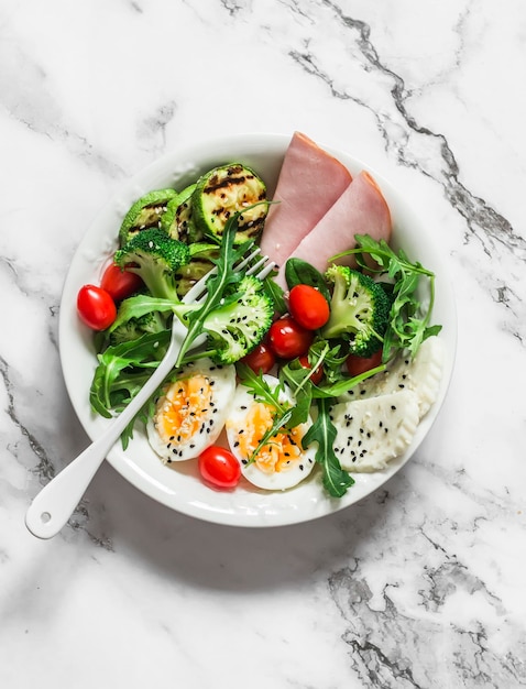 Delicioso café da manhã equilibrado tigela de presunto ovo cozido grelhado salada verde de abobrinha em uma tigela em uma vista superior de fundo claro