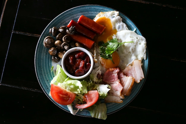 Delicioso café da manhã inglês com ovos fritos, salsichas, feijões, cogumelos, tomate e bacon, vista superior