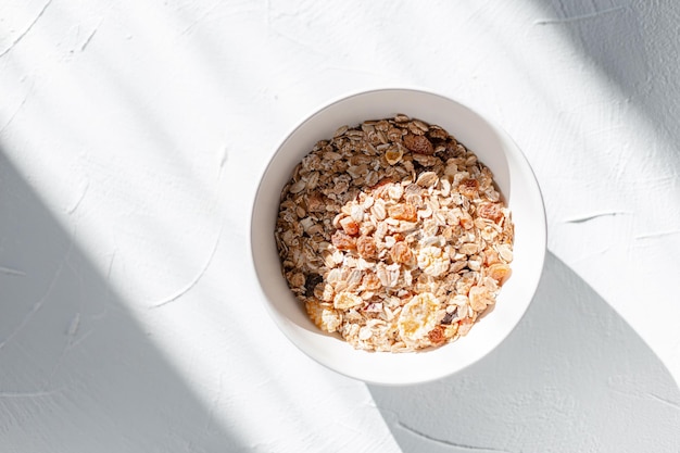 Delicioso café da manhã saudável muesli com aveia crua, frutas secas e nozes em fundo branco na manhã ensolarada com luz. comida vegana, vista de cima