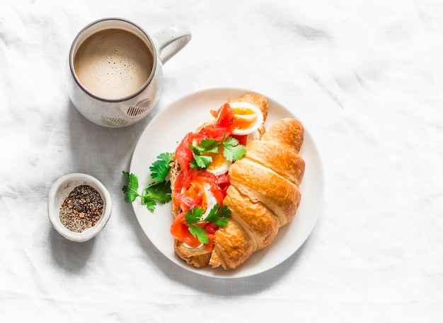 Delicioso café de desayuno brunch con sándwich de crema y croissant con salmón de queso crema y huevo hervido en una vista superior de fondo claro