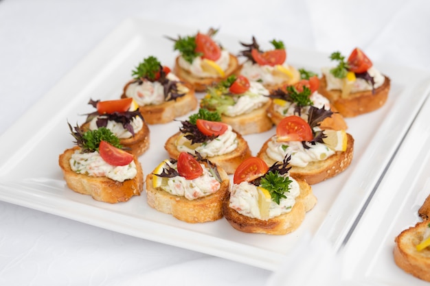 Delicioso canapé con salchichas y tomate. Canapés en platos de cerámica blanca en la recepción de la boda.