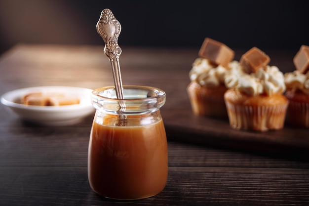 Delicioso caramelo salado con cuchara de tarro de cristal en la mesa de madera y pastelitos en el fondo