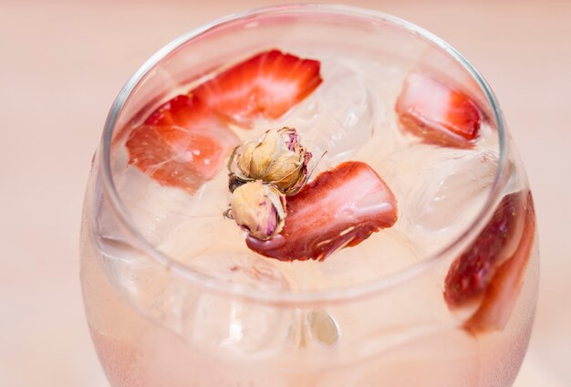 Delicioso cóctel Gin Tonic decorado con rollo de canela fresa y menta sobre un fondo rosa