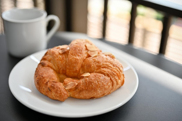 Delicioso croissant francés recién hecho con una rodaja de almendras en un plato blanco servido con café caliente