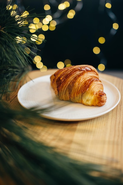 Un delicioso croissant en una mesa en una cafetería decorada con luces navideñas festivas