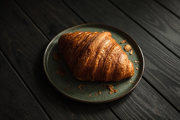 Un delicioso croissant recién horneado en un plato sobre una mesa de madera con un estilo oscuro y cambiante con enfoque selectivo de luz natural