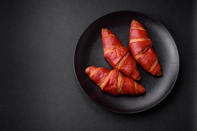 Delicioso croissant rojo dulce y crujiente con relleno de crema sobre fondo de hormigón de textura oscura