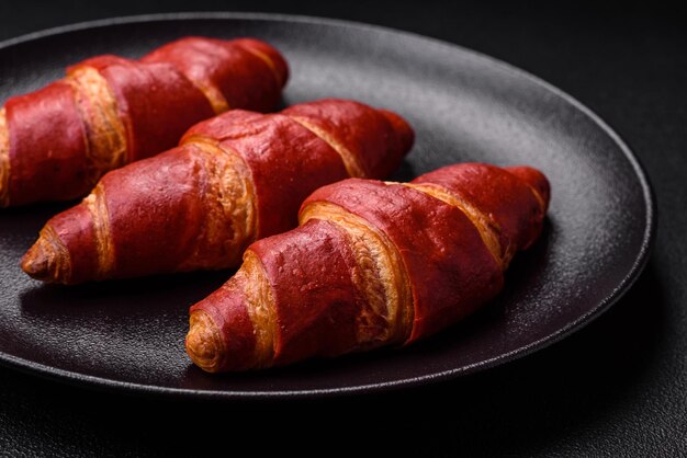 Delicioso croissant rojo dulce y crujiente con relleno de crema sobre fondo de hormigón de textura oscura