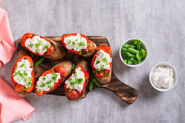 Delicioso crostini con tomates horneados pimientos ricotta y hierbas en una vista superior de tablero de madera