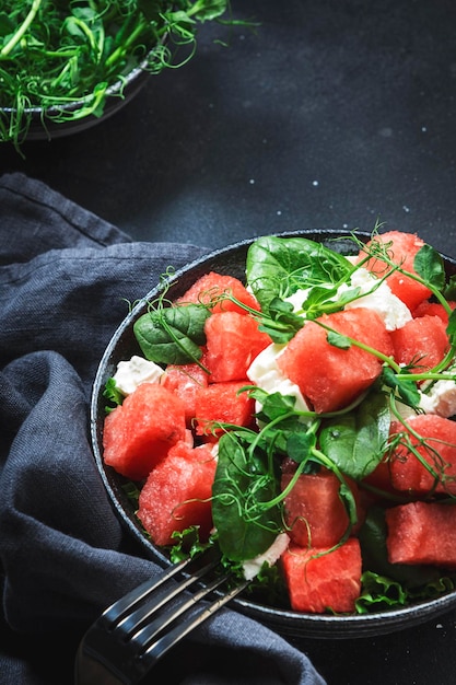 Delicioso cuenco de ensalada de sandía de verano con espinacas de queso feta y brotes de guisantes en el espacio negativo de la vista superior del fondo de la mesa gris