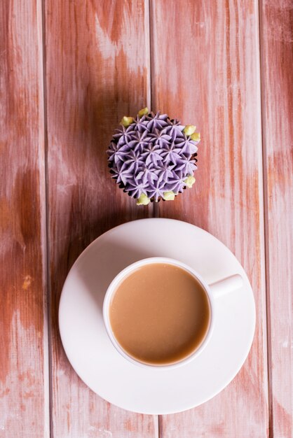 Delicioso cupcake de chocolate con crema y café fragante con leche sobre una mesa de madera blanca.