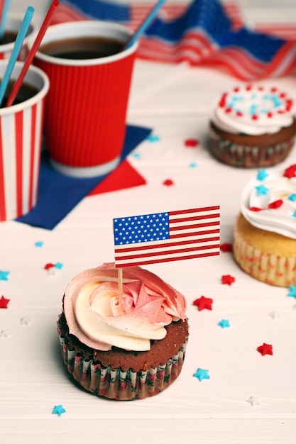 Delicioso cupcake con decoración de bandera y bebida sobre fondo blanco de madera