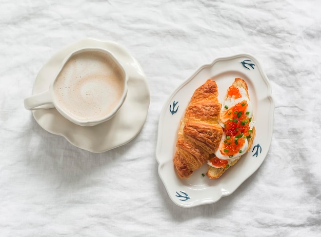 Delicioso desayuno almuerzo bocadillo capuchino y croissant queso cottage huevo sándwich de caviar rojo en un fondo claro vista superior