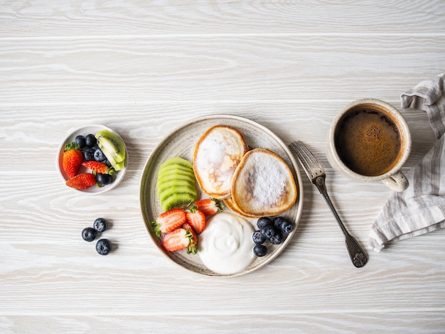 Delicioso desayuno: buñuelos de panqueques, espolvoreados con azúcar en polvo con frutas y bayas y crema agria