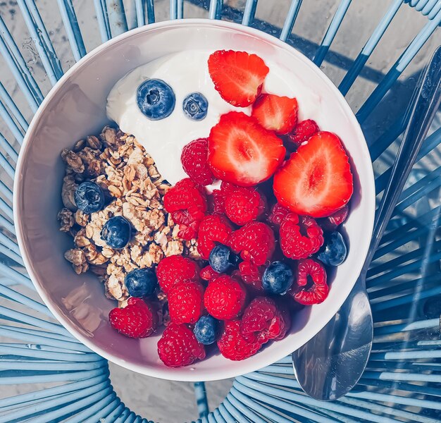 Delicioso desayuno con cereales, yogur, fresas, frambuesas y arándanos en el jardín al aire libre, comida y dieta saludables.