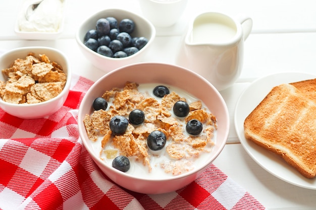 Delicioso desayuno de copos de trigo integral con leche arándanos y tostadas closeup sobre mesa de madera Concepto de dieta y comida sana