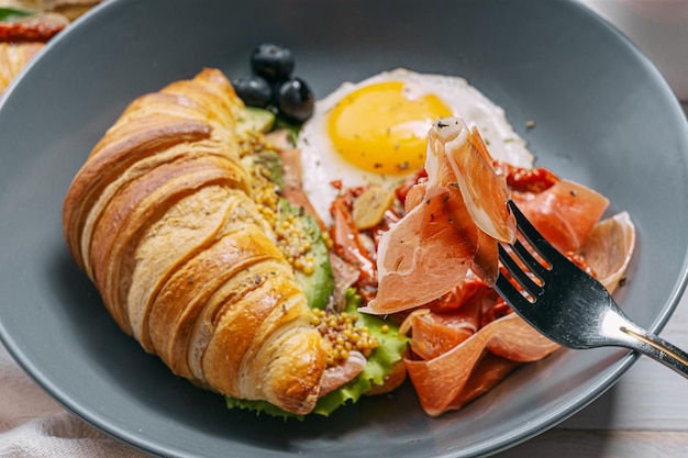 Delicioso desayuno croissant relleno de ricota y aguacate con tomates secos trozos de jamón huevo frito