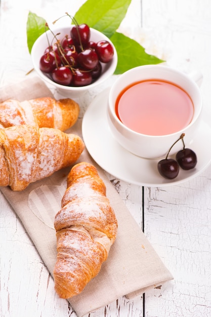 Delicioso desayuno con croissants frescos y cerezas maduras sobre fondo blanco de madera