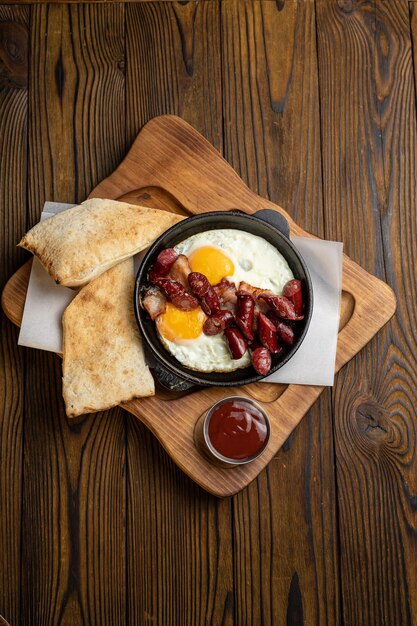 delicioso desayuno con huevo y salchichas en una sartén sobre una mesa de madera