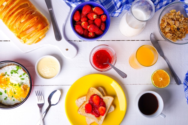 Delicioso desayuno con mermelada de fresa, jugo de naranja, cereales y huevo en la mesa blanca