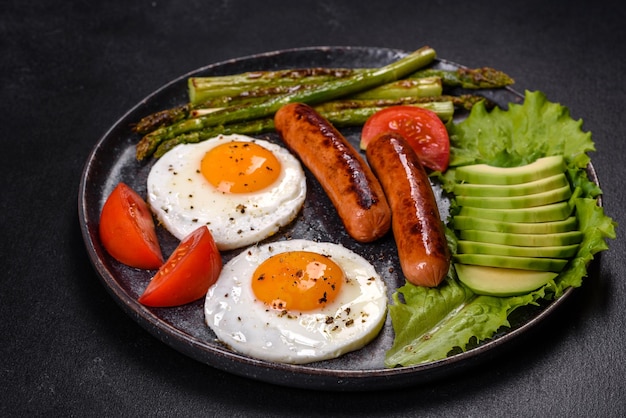 Un delicioso desayuno nutritivo con huevos fritos, salchichas, espárragos, tomates, aguacate, especias y hierbas.