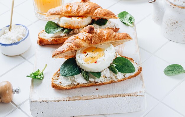 Delicioso desayuno con sándwiches de croissant con espinacas de huevo frito y café y jugo de naranja en