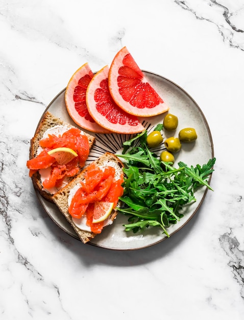 Delicioso desayuno snack tapas salmón queso crema grano pan sándwiches rúcula aceitunas rodajas de pomelo sobre un fondo claro vista superior