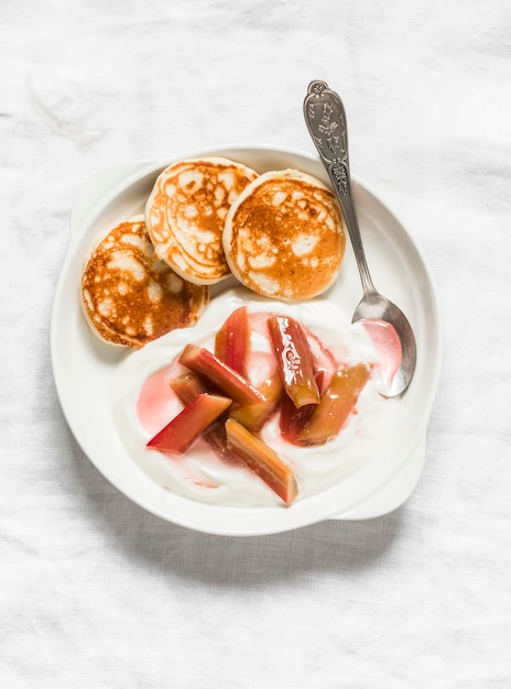 Delicioso desayuno yogur griego con salsa de ruibarbo y mini crepes en una vista superior de fondo claro