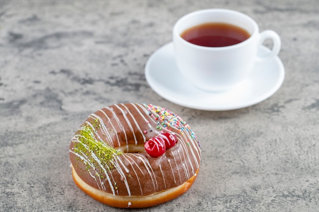 Delicioso donut com cobertura de chocolate e uma xícara de chá no fundo de pedra.