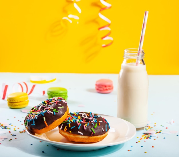 Delicioso donut con glaseado de chocolate y vela de cumpleaños con botella de leche y macarrones al fondo.