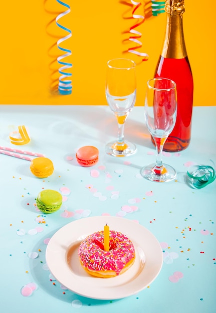 Delicioso donut con glaseado rosa y botella de velas de copas de vino y macarrones en el fondo Concepto de cumpleaños