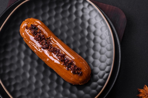 Delicioso eclair fresco com creme de chocolate em uma placa de cerâmica preta sobre um fundo escuro de concreto