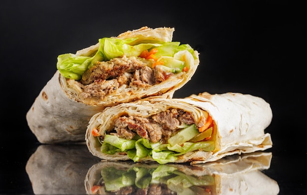 Delicioso envoltorio de shawarma con carne a la parrilla, lechuga, verduras y salsa sobre fondo negro