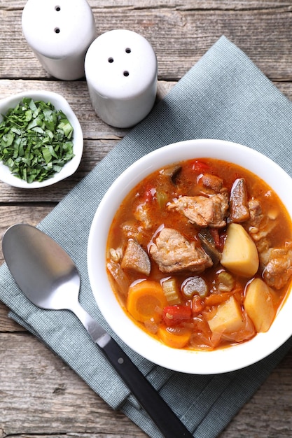 Delicioso estofado con verduras en un cuenco de perejil y cuchara en una mesa de madera