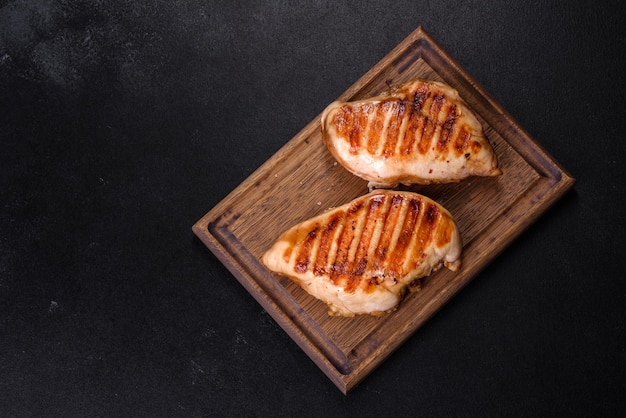 Delicioso filé de frango grelhado fresco com especiarias e ervas em um fundo escuro de concreto Um prato cozido sobre fogo