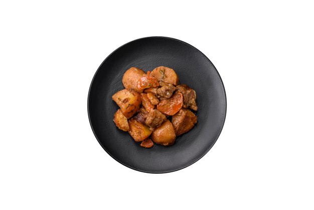 Delicioso guiso recién cocinado con carne de cerdo o ternera con patatas, zanahorias, especias y hierbas sobre un fondo de hormigón oscuro