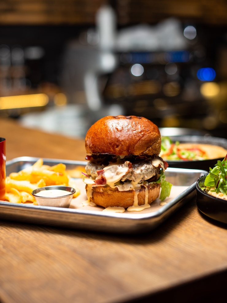 Foto delicioso hambúrguer caseiro grelhado com carne, queijo, bacon e molho na mesa de madeira com espaço de cópia. mãos segurando hambúrgueres com batatas fritas e cerveja. grupo de amigos comendo fast food